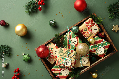 Advent calendar gifts in wooden box with festive Xmas ornaments and pine branches on green background photo