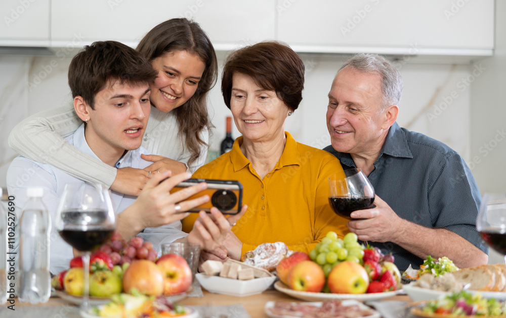 Happy bonding family looking at cellphone screen, laughing at funny video or photos in social networks, having fun at home Happy bonding family looking at cellphone screen, laughing at funny video or photos in social networks, having fun at home