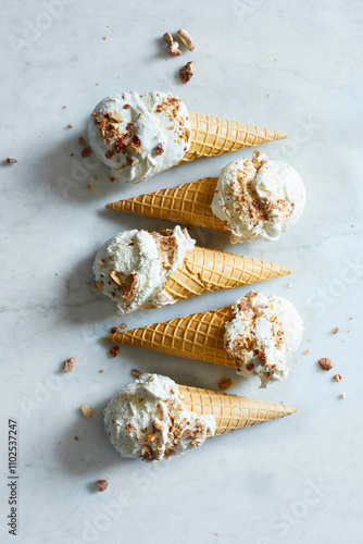 Four crispy ice cream cones filled with white homemade ice cream, and roasted almonds from above on a white marble background photo