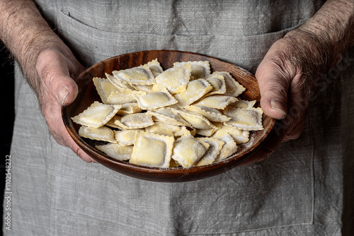 The skilled hands of a chef hold a wooden plate, containing raw ravioli, fresh and expertly shaped, ready to be cooked. photo