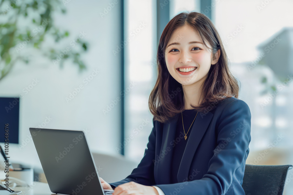 Happy young professional asian woman in formal attire working on a laptop at a bright, modern office desk with natural light. Happy young professional asian woman in formal attire working on a laptop at a bright, modern office desk with natural light.
