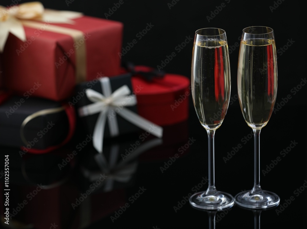 Delicious champagne in glasses and Christmas presents on black mirror surface, closeup. Space for text Delicious champagne in glasses and Christmas presents on black mirror surface, closeup. Space for text
