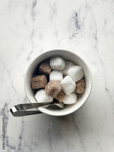  a small white bowl containing an assortment of sugar cubes. The cubes are both white and brown, suggesting a mix of refined white sugar and unrefined or raw brown sugar.