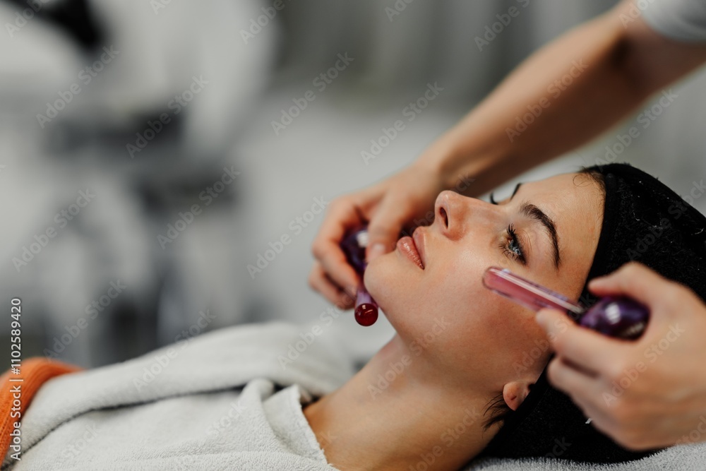 Woman receiving a facial treatment with a roller tool in a spa setting Woman receiving a facial treatment with a roller tool in a spa setting
