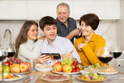 Happy parents and their children look at and discuss photos of them together on a smartphone screen