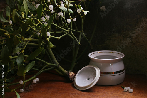 White porcelain sugar bowl and mistletoe on table against old unpainted wall photo