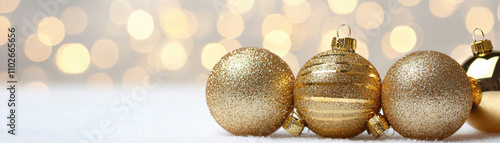 A trio of shimmering gold Christmas ornaments rests on a soft surface, with a blurred, sparkling background creating a festive atmosphere.