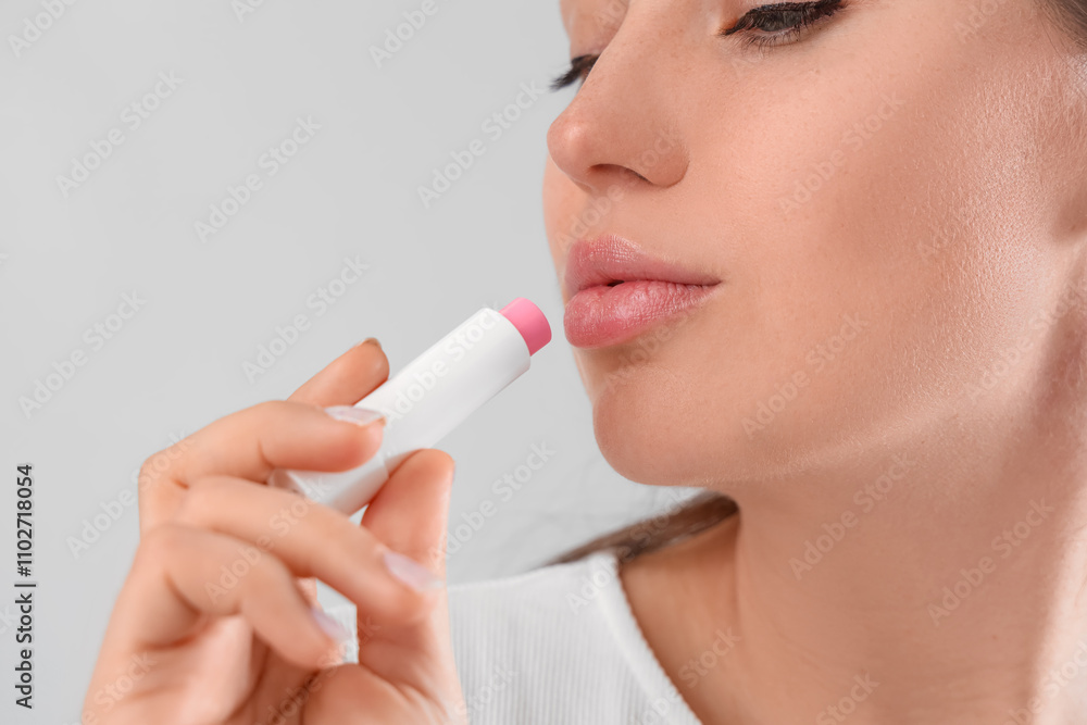 Young woman applying lip balm on light background, closeup Young woman applying lip balm on light background, closeup