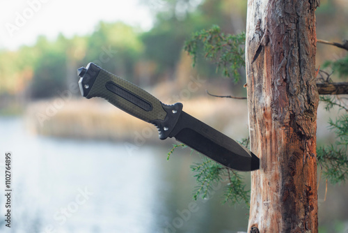 Tactical knife with a green handle in the forest. Tool against the natural leather.