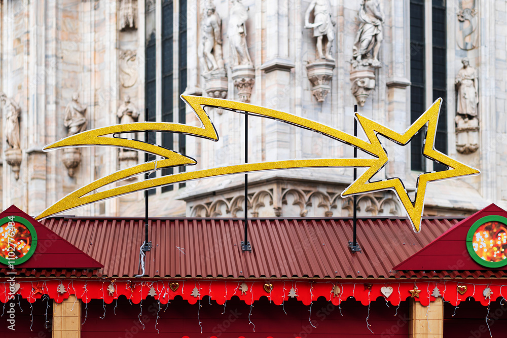 Obraz premium Large golden shooting star decoration is displayed above festive holiday market stalls. Market is set against backdrop of ornate historical building, creating charming holiday scene in city