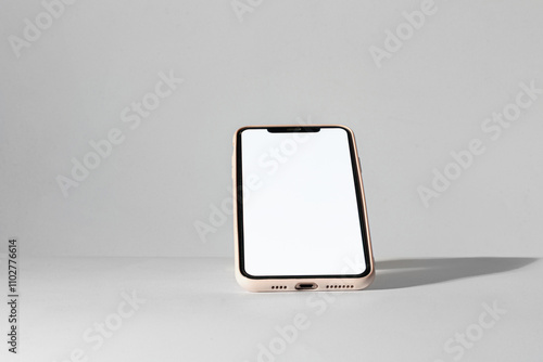 Valokuva A smartphone with a blank white screen is tilted upright on a flat surface, illuminated by soft, natural light