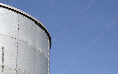 Large metal storage water tank against a clear blue sky abstract