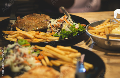 Vegetable salad and french fries and steak in a black plate on a wooden table. Select focus