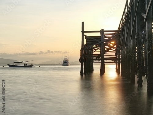 A weathered wooden pier extends into the water at sunrise, with barnacles clinging to the support posts. photo