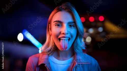 Young woman sticking her tongue out at night with colorful city lights in background.  Playful, irreverent and rebellious attitude while having fun. photo