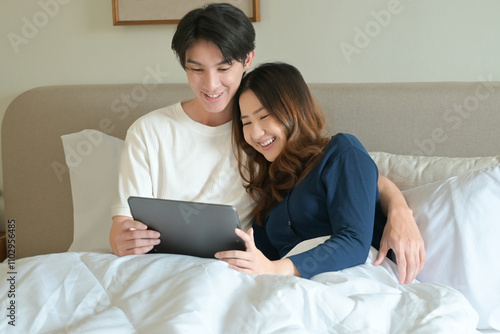 A man and woman are lying in bed together, with the man holding a tablet.