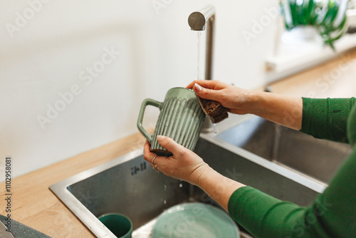 Cleaning, woman in green dress with green ceramic cup in kitchen for hygiene, routine and coffee mug. Female person, washing with water for disinfecting, protection and sink at home 