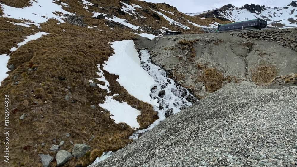 A waterfall with a snowbank on a rocky, rugged hill at The Remarkables Ski Area A waterfall with a snowbank on a rocky, rugged hill at The Remarkables Ski Area