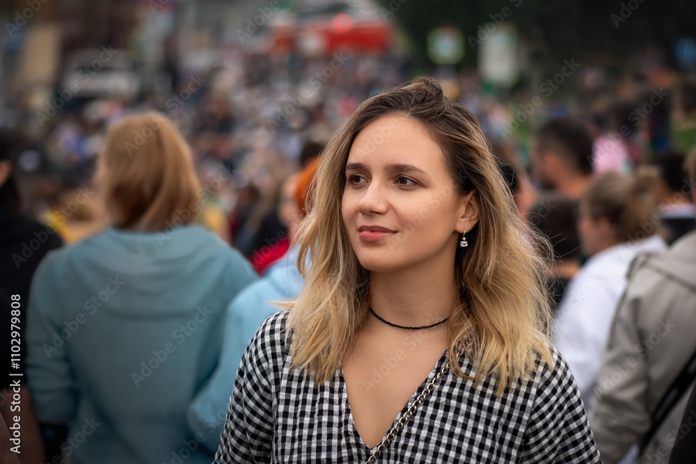 A young beautiful girl walks the floor of a city street against the traffic of the crowd. concept of going against crowd, swimming against current. A blonde against a background of many blurred people A young beautiful girl walks the floor of a city street against the traffic of the crowd. concept of going against crowd, swimming against current. A blonde against a background of many blurred people