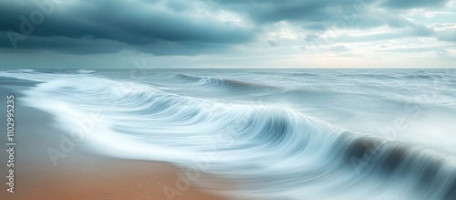 Serene long exposure seascape with gentle waves on sandy beach under moody clouds at dawn or dusk for tranquil artistic decor