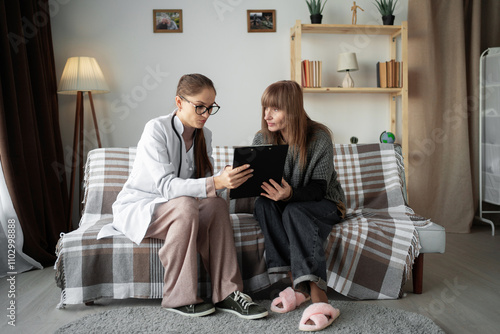 Professional doctor working with patient consulting at home showing elderly woman examination results and prescriptions written on clipboard