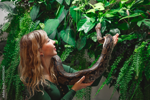 Pretty young woman holding a snake at a reptile encounter, symbolizing an exciting and educational animal interaction, against floral wall
