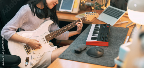 Young asian woman composer playing guitar music with digital technology at home studio photo