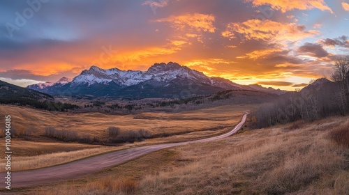 A breathtaking sunrise over majestic mountains with a winding road cutting through serene grasslands and vibrant skies.