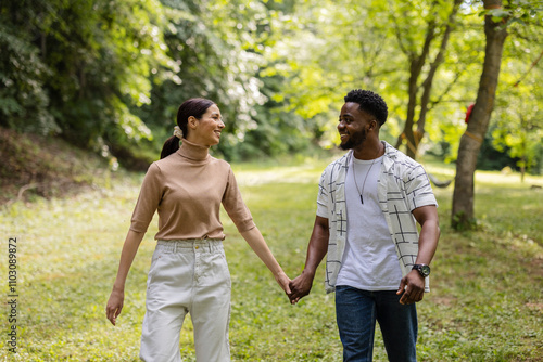 Happy multiracial couple holding hands and walking in park