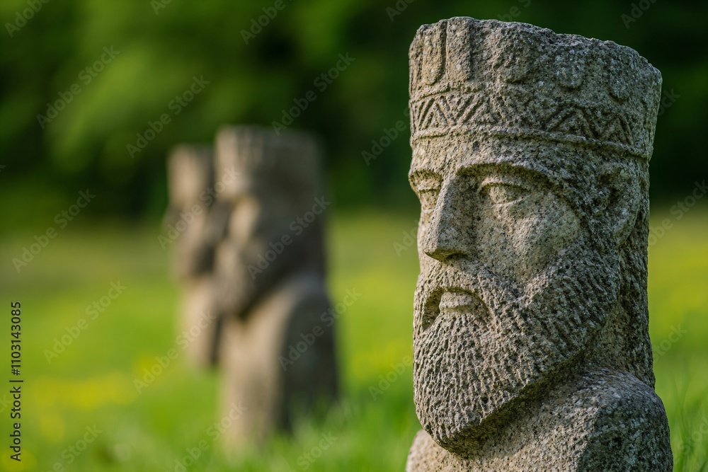 Ancient stone sculptures in park garden setting. Historical carved monuments with ornate details and crown-like headpieces against blurred green background with copy space Ancient stone sculptures in park garden setting. Historical carved monuments with ornate details and crown-like headpieces against blurred green background with copy space