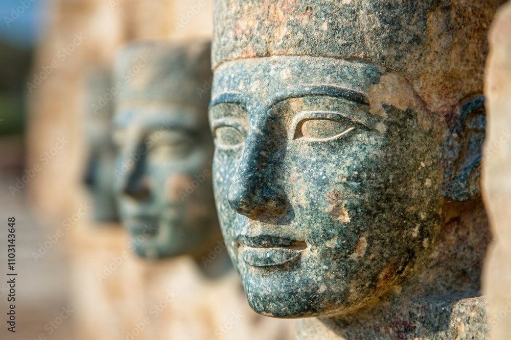 Fototapeta premium Ancient Egyptian stone statues with weathered patina. Archaeological artifacts showing traditional sculptural heads. Historical art exhibition display with blur effect and copy space