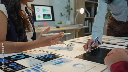 Team of business people or financial analysts working together, discussing using tablets and laptops and graphing data, planning, explaining, presenting project analysis results in modern office.