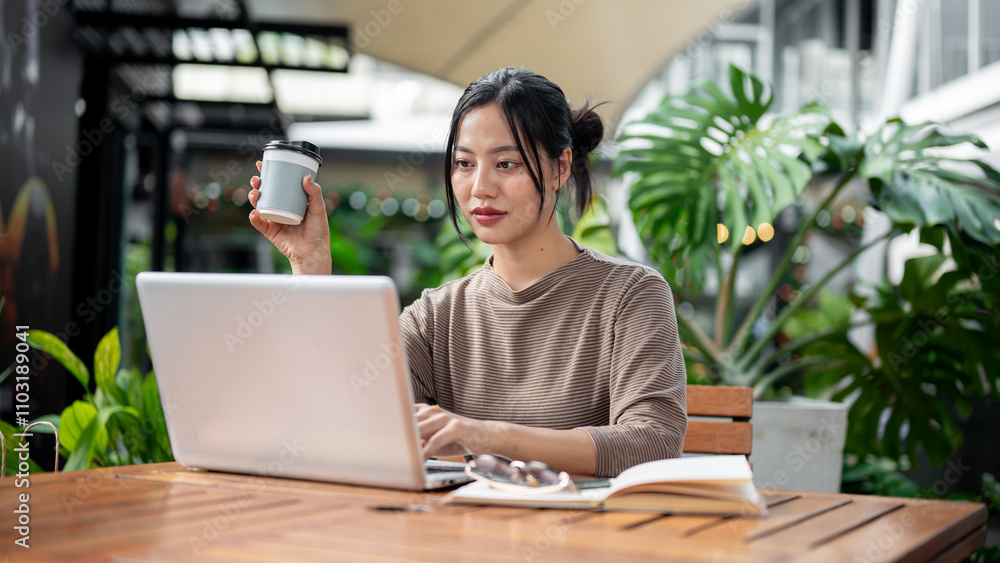 An attractive Asian woman sitting at an outdoor table of a cafe, working remotely. An attractive Asian woman sitting at an outdoor table of a cafe, working remotely.