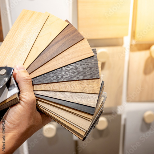 Designer hand choosing sample of wood laminated from natural collection in material showroom. Set of wooden veneer texture or MDF board swatch fan for interior finishing or furniture design photo