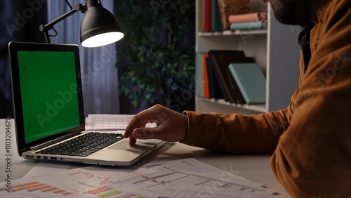 Obraz na plátně Adult business man sitting at desk working late at night in dark office, using laptop with chroma key green screen background, workspace mockup