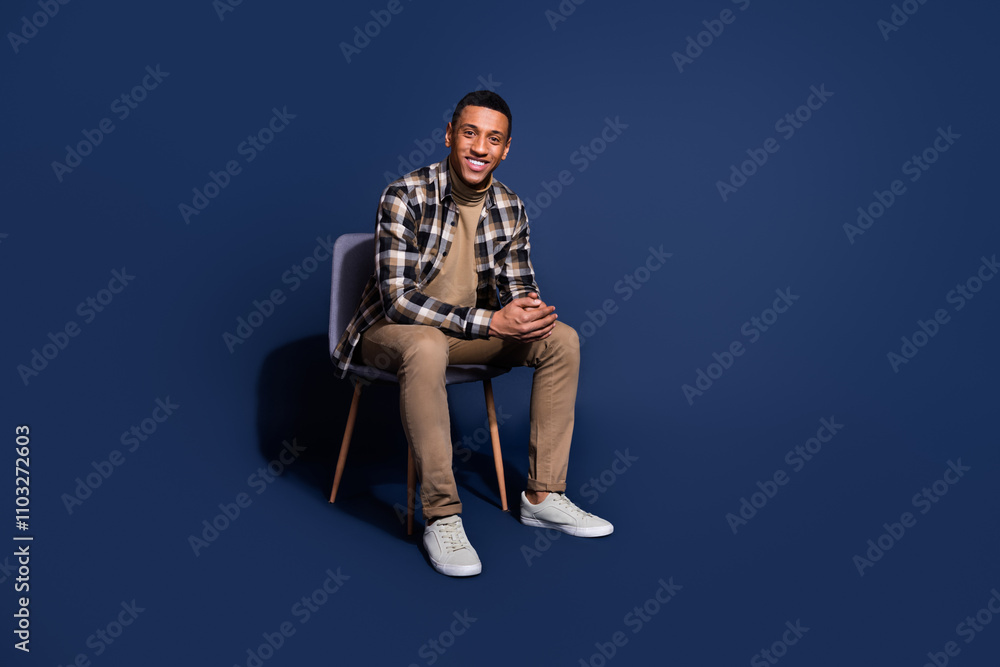 Fototapeta premium Full length photo of cheerful positive guy dressed plaid shirt sitting chair emtpy space isolated blue color background