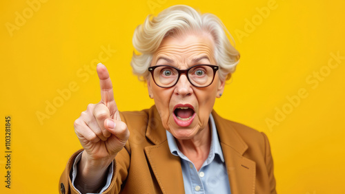 angry granny threatens with her finger. elderly woman on yellow background. grandma looks at the camera and hand pointing