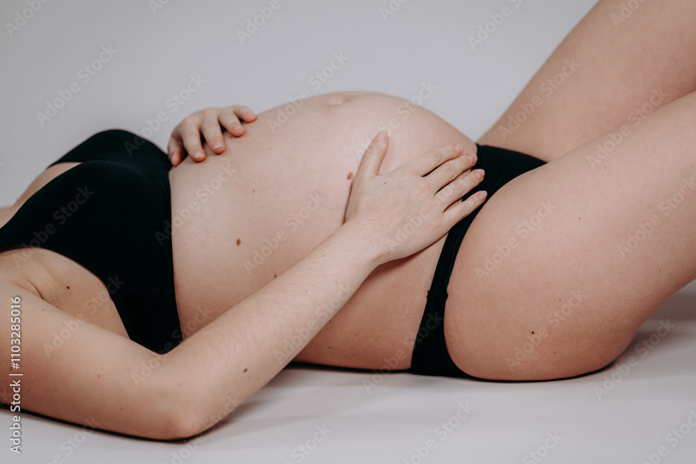 Fototapeta premium Ciężarna kobieta w czarnej bieliźnie leży na plecach