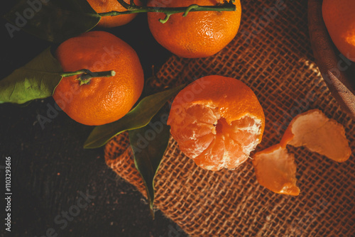 Rustic still life of peeled and whole tangerines on a burlap background, illuminated by warm natural light. Perfect for food photography, seasonal visuals, and organic themes photo