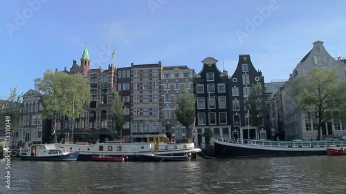 Travelling along an Amsterdam canal past historic facades and houseboats. Amsterdam, The Netherlands.