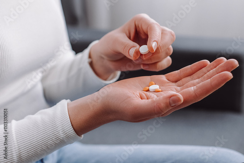Close up of female hand holding pills sitting on couch, painkiller medicine from stomach pain, headache, pain for treatment, take drug or vitamin at home, health care concept