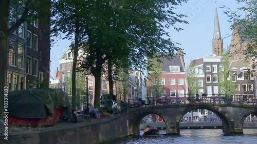 Travelling along a canal in Amsterdam with three-arched bridge in the background. Amsterdam, The Netherlands.