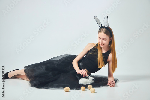 A young beautiful girl in a bunny costume and black clothes on a clean white background. In the hands of a small rabbit photo