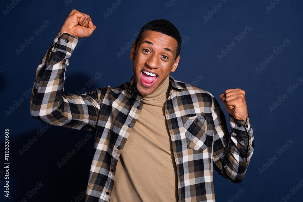 Photo portrait of attractive young man raise fists winning dressed stylish checkered clothes isolated on dark blue color background Photo portrait of attractive young man raise fists winning dressed stylish checkered clothes isolated on dark blue color background