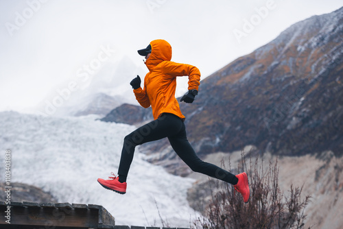 Fitness woman trail runner running in grassland with snow capped mountains in the background photo