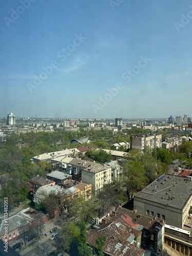 Panoramic urban view of a cityscape with residential buildings, greenery, and a clear blue sky on a sunny day