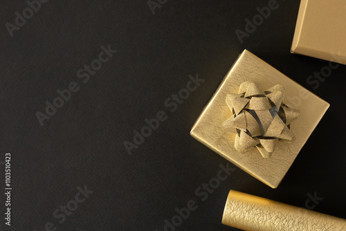 Golden gift box with gold bow on black background and gold gift wrapping paper. Top view, flat lay with copy space. Concept for holiday.