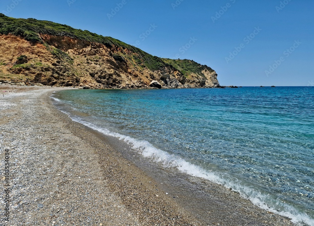Obraz premium Pebble turquoise beach of Xanemos, above which planes take off and land. Greek island of Skiathos, Europe.
