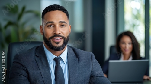 Confident African American business executive in formal suit and tie sitting at desk in modern office using laptop computer Portrait of a professional successful manager or entrepreneur