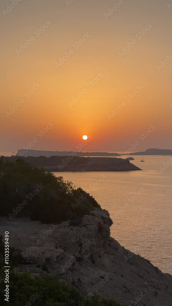A beautiful sunset over the ocean with a small island in the distance. The sky is a mix of orange and pink hues, creating a serene and peaceful atmosphere